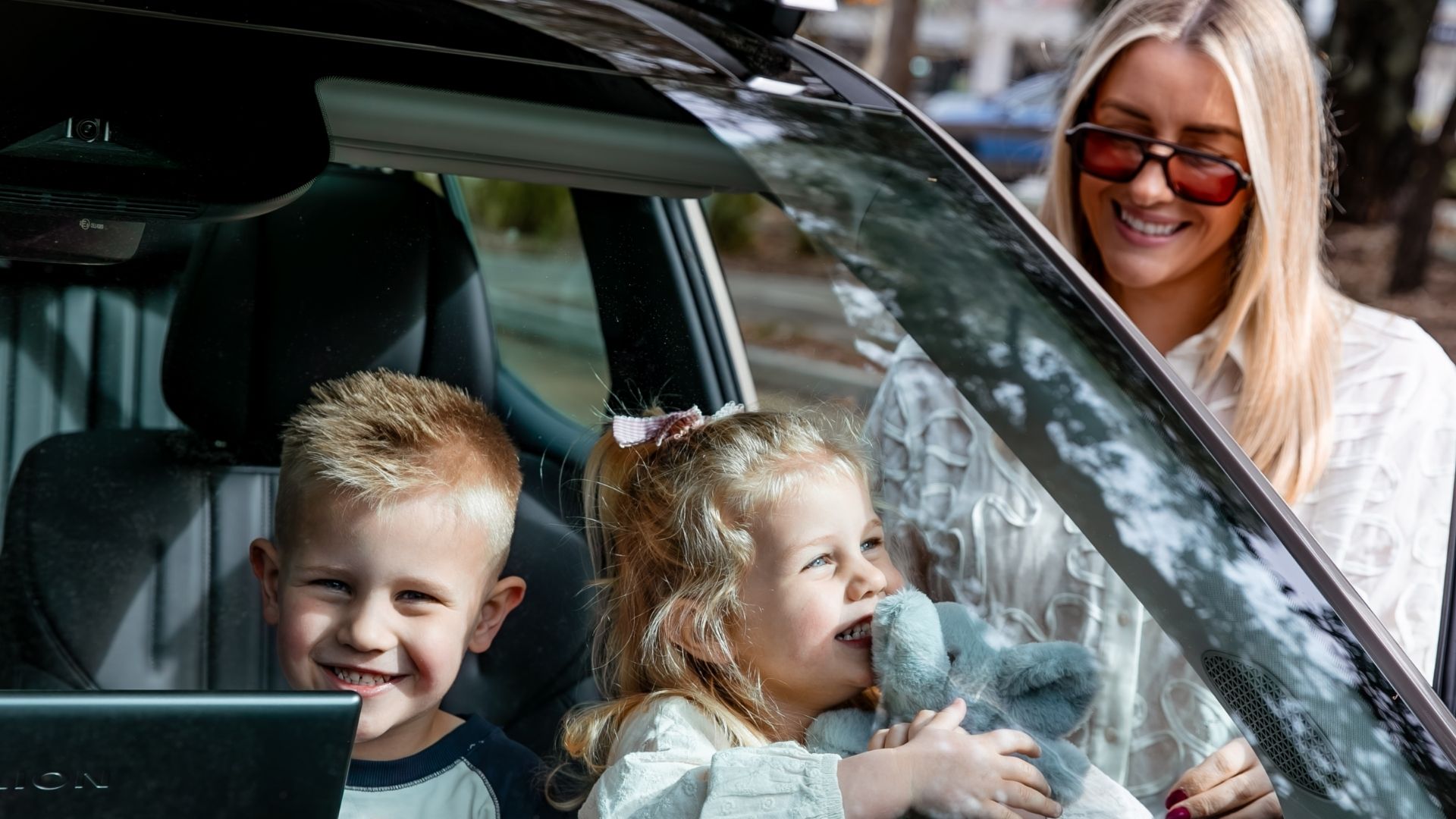 Two children smiling in the back seat of a car, ready for a family summer road trip.