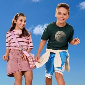 Two smiling children model colourful casual summer outfits against a bright blue sky backdrop.
