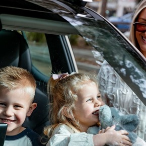 Two children smiling in the back seat of a car, ready for a family summer road trip.